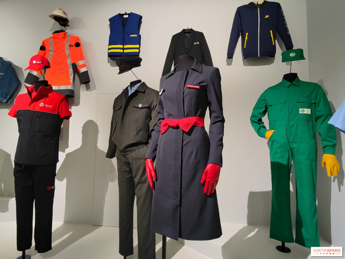 salle aux murs blancs exposant plusieurs vêtements de travailleurs 